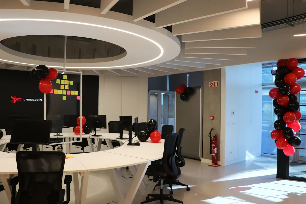 Bright open office space featuring a large circular white desk with computers, black office chairs, and festive red and black balloons.